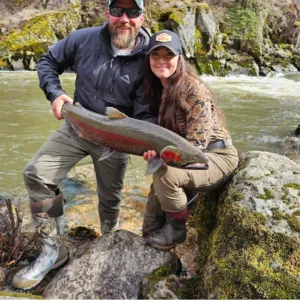 a man and a women is wearing kalkal rubber boots in the lake, holding a big fish they just caught
