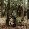a man is standing beside a tree with his gun and plan to climb and hunt on the tree