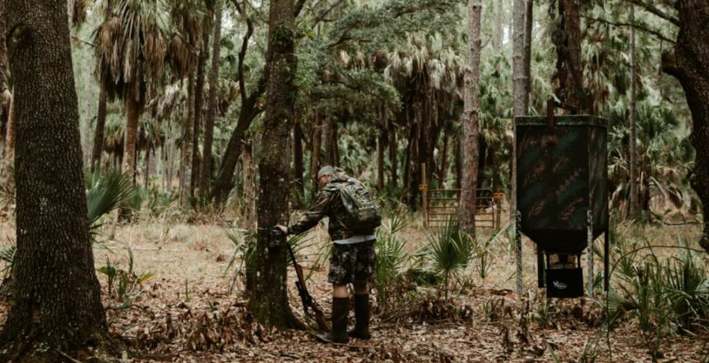 a man is standing beside a tree with his gun and plan to climb and hunt on the tree