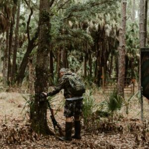 a man is standing beside a tree with his gun and plan to climb and hunt on the tree